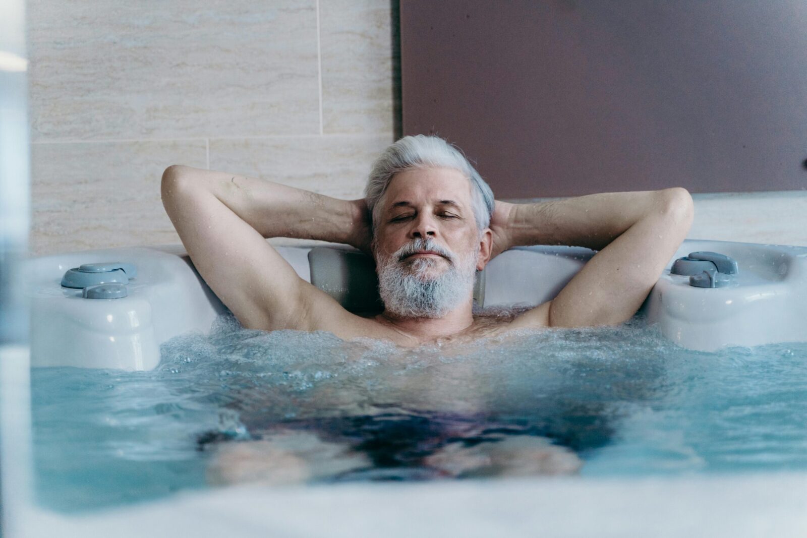 Elderly man with grey hair enjoying relaxation in an indoor jacuzzi.